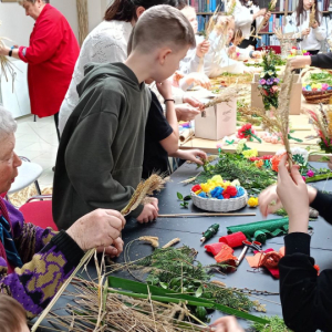Przy stole na którym leżą różne materiały dzieci oraz prowadzące wykonują palmy wielkanocne.