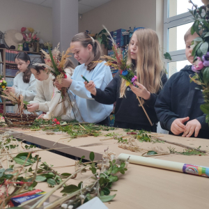 Grupa dzieci stoi przy stole, trzymając w rękach palmy ,na stole przed nimi leżą różne materiały.