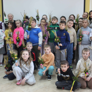 Dzieci oraz prowadzące pozują do zdjęcia trzymając w rękach wykonane podczas zajęć palmy wielkanocne.