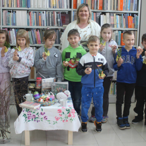 Dzieci wraz z nauczycielką pozują do zdjęcia z wykonanymi podczas zajęć wielkanocnymi kurczakami.