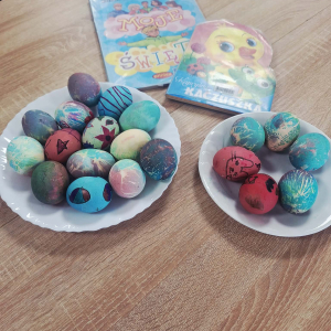 Na dwóch talerzach leżą kolorowe pisanki, obok leżą dwie książki.