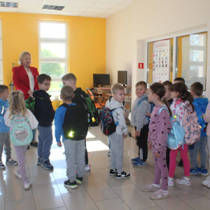 Dzieci stoja wokół bibliotekarki w sali z komputerami
