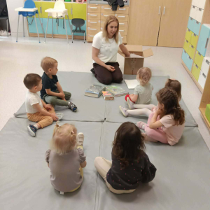 Na materacu w okręgu siedzą dzieci wraz z prowadzącą ,przed nimi leżą książki.