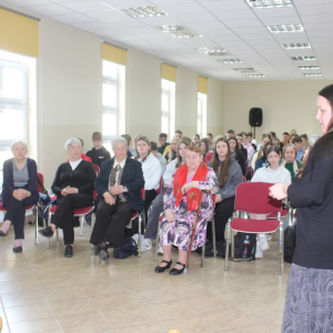 Na sali siedzą uczestnicy spotkania autorskiego przed nimi stoi pisarka.