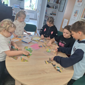 Dzieci stoją przy stole , na którym rozłożone są kolorowe puzzle, dzieci próbują je ułożyć.