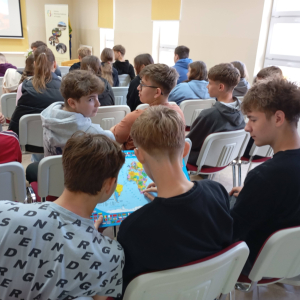 Uczestnicy spotkania siedzą na krzesłach, dwóch chłopców trzyma w rękach mapę.