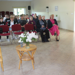 Uczestnicy Spotkania siedzą na krzesłach patrzą na autorkę prac, która opowiada o swojej wystawie fotograficznej.
