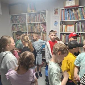 Grupa dzieci w jednym z pomieszczeń bibliotecznych ogląda ksiażki.