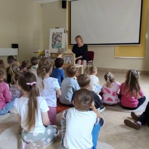 Grupa dzieci siedzi na podłodze przed bibliotekarką