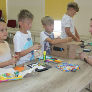 Czworo dzieci przy stole podczas zajęć plastycznych rozmawiają z prowadzącą.”