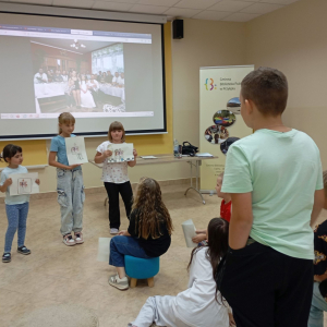 Trzy dziewczynki prezentują swoje prace grupie uczestników