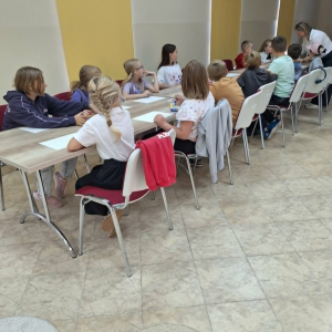 Dzieci rysują podczas warsztatów w bibliotece pod okiem prowadzącej