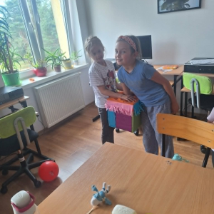 Jedna z dziewczynek trzyma w rękach kolorowe pudełko,druga wkłada do niego rękę.