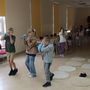 Uczestnicy zajęć chodzą po sali konferencyjnej, jednym okiem patrzą przez tyby wykonane z kolorowego papieru.