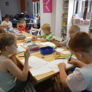 Grupa dzieci przy stole projektuje pocztówki.