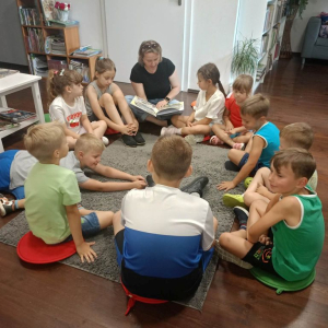 Bibliotekarka czyta dzieciom siedzącym w kole książkę o ekologii.