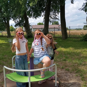 Trzy dziewczynki stoją na karuzeli, patrzą przez własnoręcznie wykonane lornetki