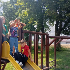 Czterech chłopców stoi na podeście zjeżdżalni, jeden patrzy przez własnoręcznie zrobioną lornetkę