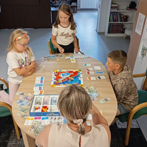 Troje dzieci gra z bibliotekarką w planszówkę