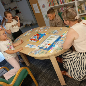 Troje dzieci gra z bibliotekarką w planszówkę