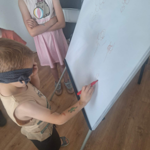 Chłopiec rysyje coś na dużym arkuszu papieru z zasłoniętymi oczami.