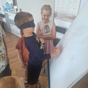 Chłopiec rysyje coś na dużym arkuszu papieru z zasłoniętymi oczami.