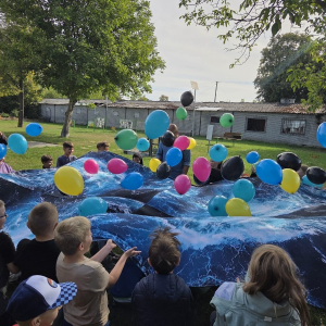 Uczestnicy spotkania na placu bibliotecznym podrzucają na dużej chuście kolorowe balony.