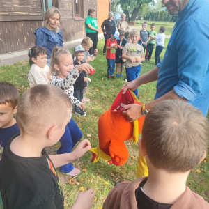 Dzieci wrzucają smakołyki do brzucha pluszowej kury, którą trzyma pisarz.