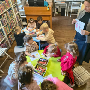 Bibliotekarka pokazuje grupie maluchów jak wykonać zadanie rysunkowe