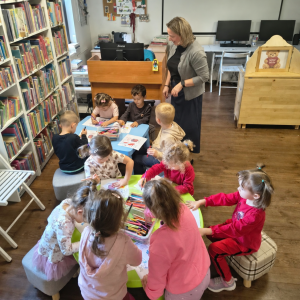 Bibliotekarka tłumaczy grupie maluchów jak wykonać zadanie rysunkowe