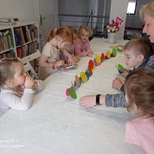 Opiekun z dziećmi siedzi razem przy stole oglądają prace plastyczne