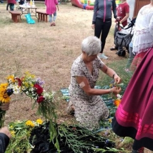 Kobieta siedzi na ziemi i wije wianek