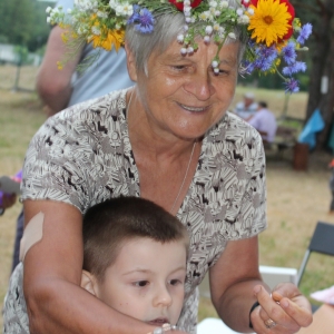 Uśmiechnięta starsza kobieta w wianku na głowie, przed sobą ma chłopca.