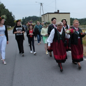 Grupa ludzi z wiankami w dłoniach w korowodzie idzie ulicą.