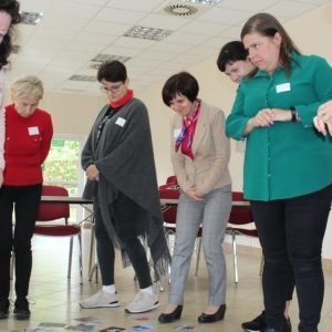 Panie bibliotekarki biorące udział w szkoleniu przyglądają się obrazkom ułożonym na podłodze.