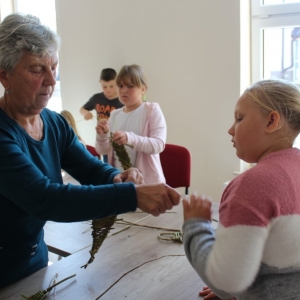 Pani pokazuje dziewczynce jak ma zaplatać wiklinę