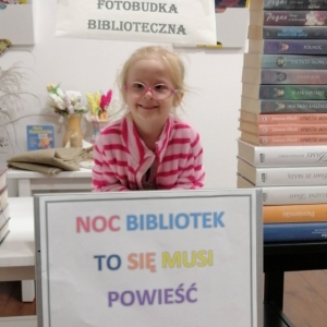 Dziewczynka o jasnych włosach w okularach w fotobudce bibliotecznej.