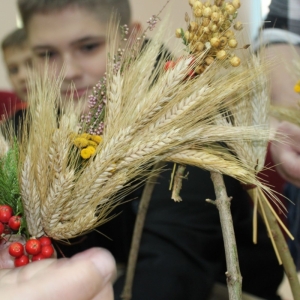 Ręce wiążą zboża, zioła, jarzębiny na stelażu.