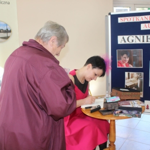 Pisarka składa autograf na książce. Starsza kobieta przygląda się pisarce.