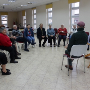 Uczestnicy warsztatów siedzą na krzesłach w półokręgu. Naprzeciwko siedzi mężczyzna.