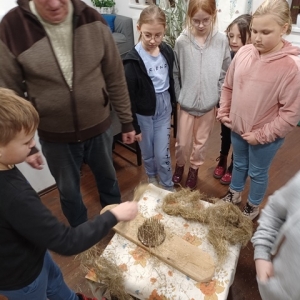 Dzieci razem z opiekunem stoją wokół stołu na którym leży czesadło