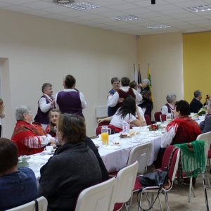 Przy stole siedzi część uczestników spotkania obok grupa tańczy