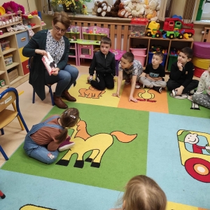 Kobieta siedzi wśród dzieci i pokazuje książkę